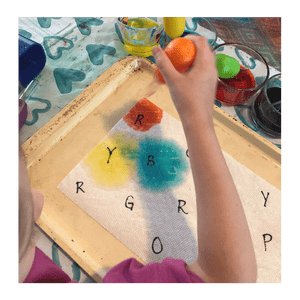 Child covering letters with colored water using an eye dropper