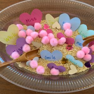 Sensory play with rhyming words: sensory tray with heart-shaped rhyming words, pom poms and utensils