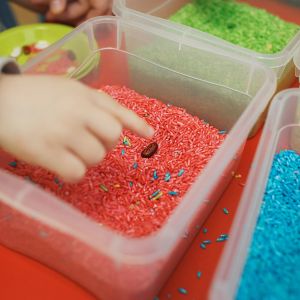 Sensory play with colored rice in bins and child putting hand into bin